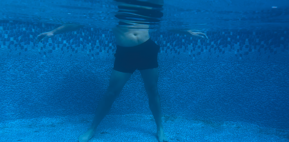 Man doing hip rotation aqua therapy exercise in a pool. Under water angle.