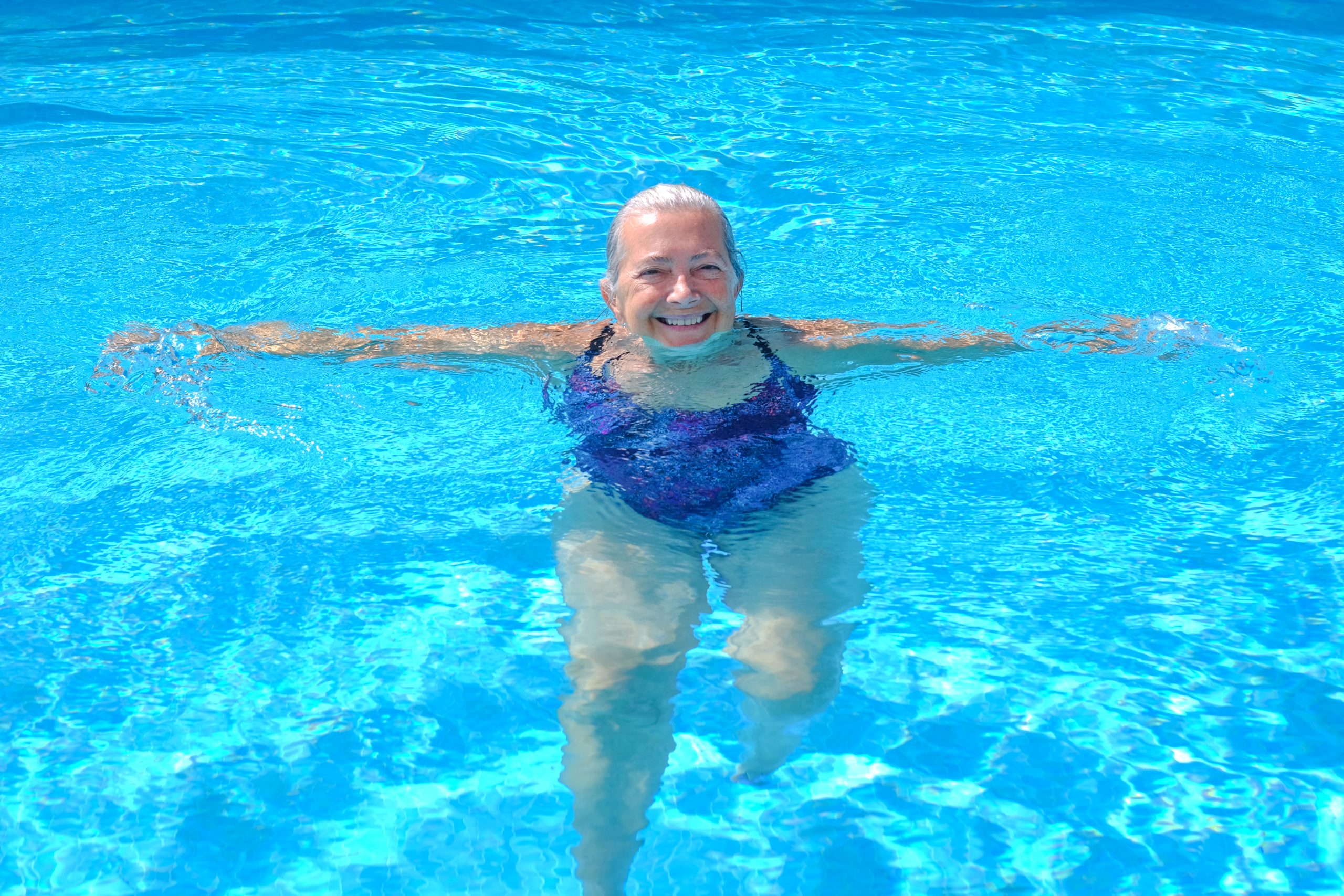 cheerful senior woman doing side arm raises in a pool
